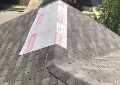 A house roof partially covered with grey asphalt shingles and a section with exposed underlayment labeled "durock" on a sunny day.